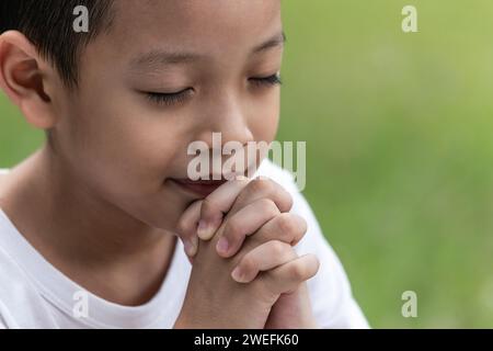 Little boy with Bible praying and close your eyes in praying. Prayer to pray. Children pray with folded hands. Stock Photo