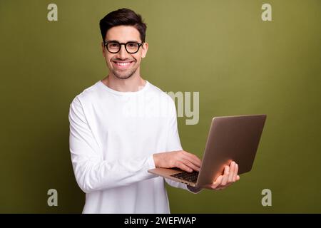 Photo of young optimistic system administrator man in white pullover typing keyboard his netbook isolated on khaki color background Stock Photo