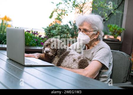 old woman wearing face mask using laptop on terrace Stock Photo