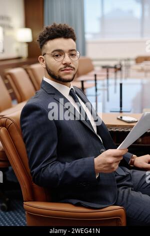 Professional lawyer sitting in armchair in conference room holding papers in hand looking at camera Stock Photo