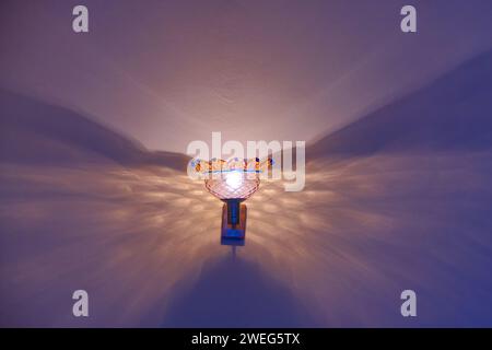 Glass blue lamp on the wall burning light and producing beautiful shadows Stock Photo