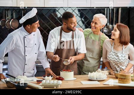 cheerful african american man in apron decorating cake and smiling at his friends and chef Stock Photo