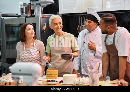 cheerful mature woman with silicone brush smiling at her diverse friends and chef in white hat Stock Photo