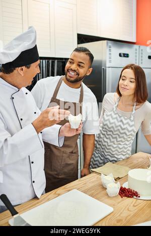 cheerful african american man in apron next to his friend smiling at mature chef during lesson Stock Photo
