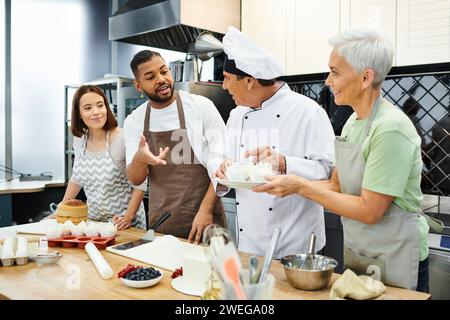 cheerful multiracial people in aprons talking to mature chef in white hat, cooking courses Stock Photo