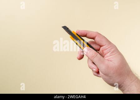 Hand holding a yellow and black metal utility knife in front of a yellow background Stock Photo