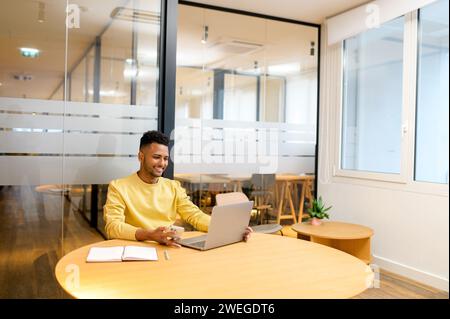 Smiling Indian man, office employee or student in casual clothes sitting at the desk, studying or working online Stock Photo