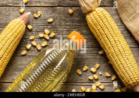 Corn oil in plastic bowl with dried corn groats and kernels on rustic backdrop. Cooking oil composition Stock Photo