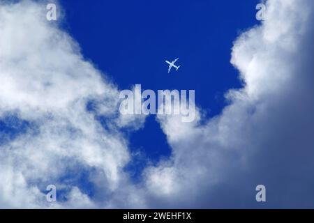 a single white passenger plane in the blue sky between clouds Stock Photo