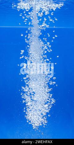 a thin jet of water penetrates the water surface and produces many air bubbles in the blue water of an aquarium Stock Photo