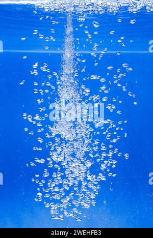 a thin jet of water penetrates the water surface and produces many air bubbles in the blue water of an aquarium Stock Photo