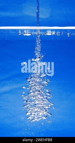 a thin jet of water penetrates the water surface and produces many air bubbles in the blue water of an aquarium Stock Photo