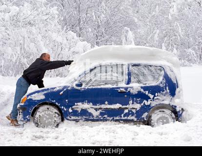 a man frees his blue compact car from half a metre of fresh snow, Munich ca. 2006, Bavaria, Germany, Europe Stock Photo