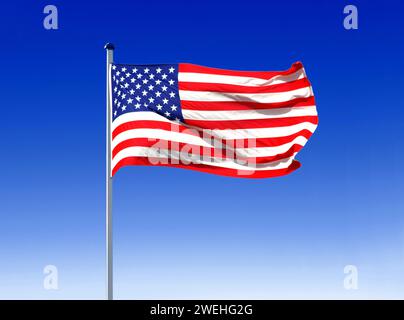 the national flag of the USA flies in the wind on a flagpole with a blue sky as a backdrop Stock Photo