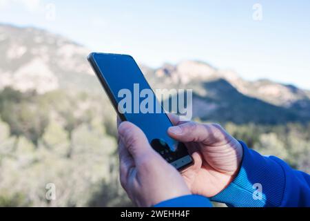 A person's Hand holding smartphone in front of mountain Stock Photo