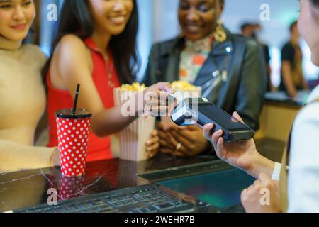Diverse group of female friends, representing different nationalities, joyfully uses credit cards to pay for movie tickets at the theater Stock Photo