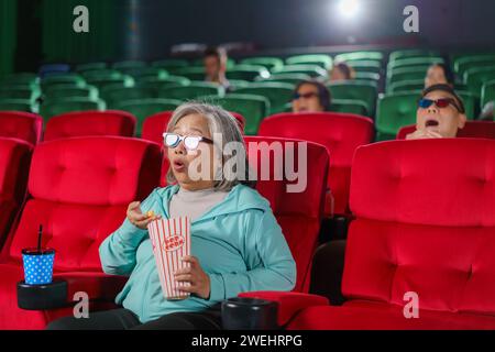 elderly Asian woman as she expresses genuine astonishment while watching a horror film in the cinema Stock Photo