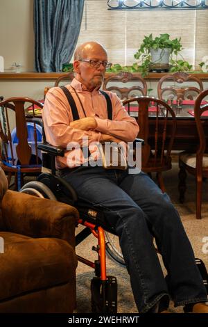 67 year old balding Caucasian handicapped senior adult man wearing glasses, sitting in a wheelchair & looking away. USA. Stock Photo