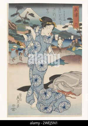 Standing woman with box, 1830 print A woman in blue kimono and box in her hands. In the background travelers at the Okitsu stopping place at the foot of Mount Fuji.  paper color woodcut standing figure - AA - female human figure Okitsu. FUJI Stock Photo