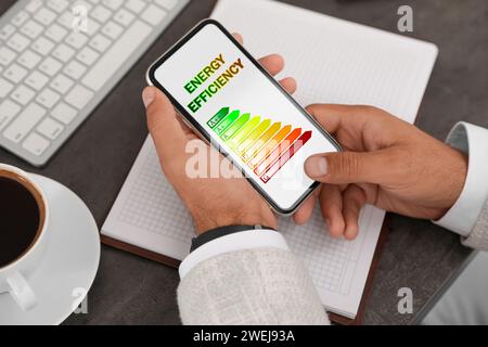 Energy efficiency. Man using smartphone with colorful rating on display at table, closeup Stock Photo