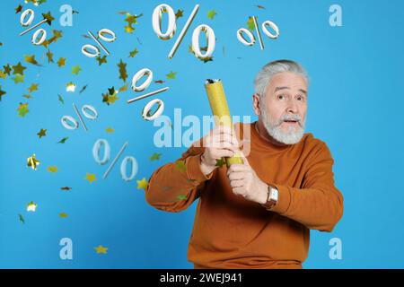 Discount offer. Senior man blowing up party popper on light blue background. Confetti and percent signs in air Stock Photo