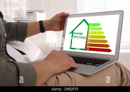 Energy efficiency. Man using laptop with colorful rating on display at home, closeup Stock Photo
