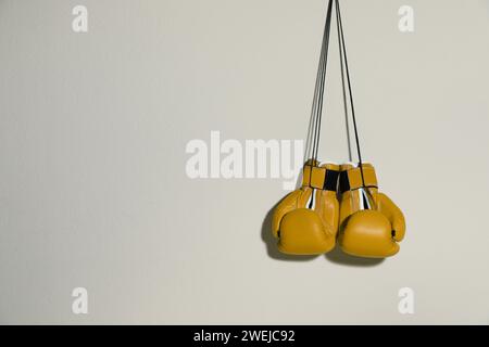 Pair of yellow boxing gloves hanging on light grey wall, space for text Stock Photo