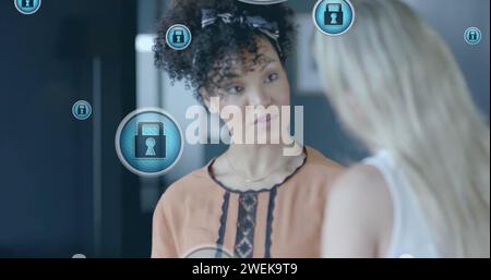 Image of padlock icons data processing over diverse businesswomen in office Stock Photo