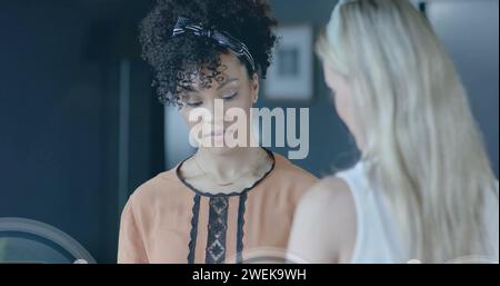 Image of padlock icons data processing over diverse businesswomen in office Stock Photo