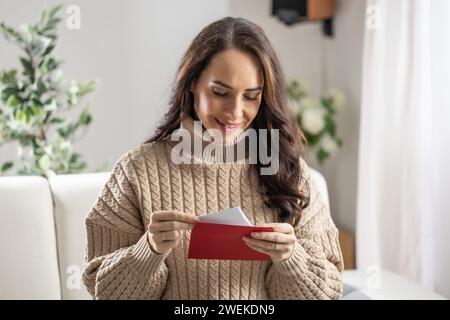 A good-looking brunette reads a love letter with a red envelope that she received from her boyfriend. Stock Photo