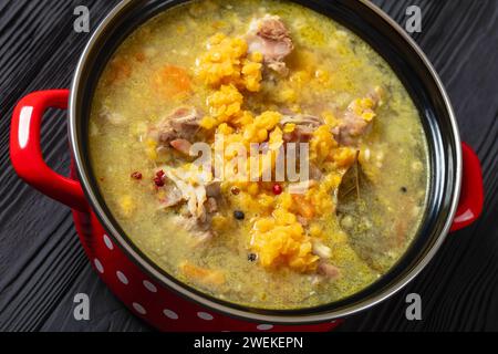 split pea and lentil soup with pork on bones and vegetables in red pot on black wooden table, close-up Stock Photo