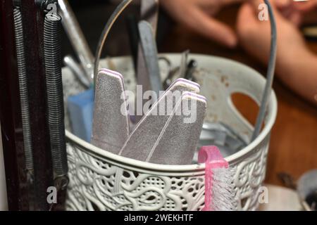 Manicure tools, nail files, tongs, brushes, tassels are stored in a plastic bucket on the table. Stock Photo