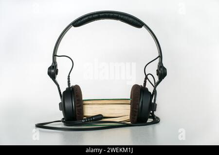 A pocket book with headphones and a mini-jack plug inserted between the pages on a light background. Concept of audiobook Stock Photo