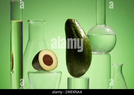 Fresh avocado and essential oil in lab glassware on green background. Research and development natural extract concept. Production of cosmetics based Stock Photo
