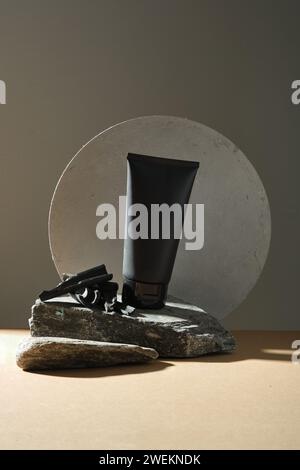 A black plastic bottle unlabeled set on stones on black background with bamboo charcoal and geometric shape. Mockup for facial cleanser of bamboo char Stock Photo