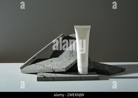 Dark rectangle stones are randomly decorated and white plastic bottle without label on black background. Minimal style, mockup for cosmetic, facial mo Stock Photo