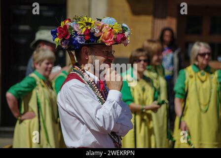 Morris Man wearing a hat decorated with flowers at a Morris Dancing convention, Northampton, UK; out of focus lady Morris Dancers to the rear Stock Photo