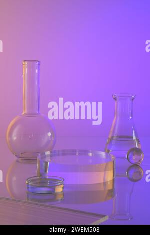 Equipment of the chemical laboratory - glass flask and petri dish containing transparent decorated on gradient background. Empty podium for cosmetic p Stock Photo