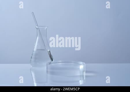 Lab theme, laboratory glassware - erlenmeyer flask containing colorless liquid with glass rod inside and transparent podium on white background. Blank Stock Photo