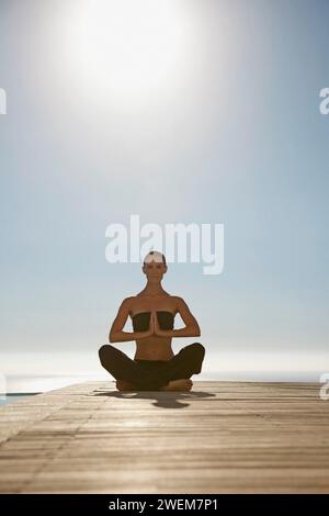 Young woman practicing yoga by a swimming pool with ocean in the background Stock Photo