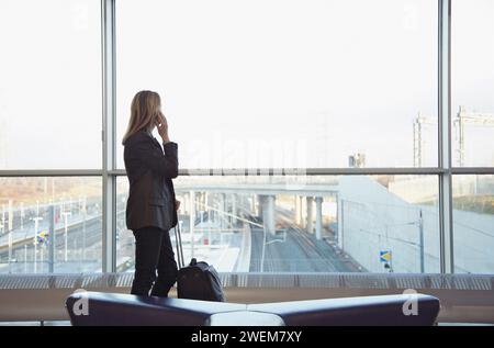 Back view of a woman using a cell phone in a train station terminal Stock Photo