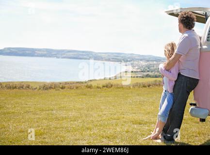 Father and Daughter Leaning on Back of Camper Van Looking at Ocean Stock Photo