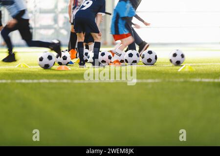 An anonymous group of children attending soccer class with coach. School children running and kicking balls on summer training camp. Football soccer c Stock Photo