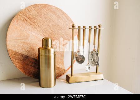 Wooden Cutting Board and Gold Cocktail Mixing Set on White Counter Stock Photo