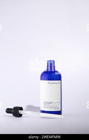 An open glass bottle of Pyunkang Yul brand moisturizing serum. Stands on a white background, next to a pipette. Stock Photo
