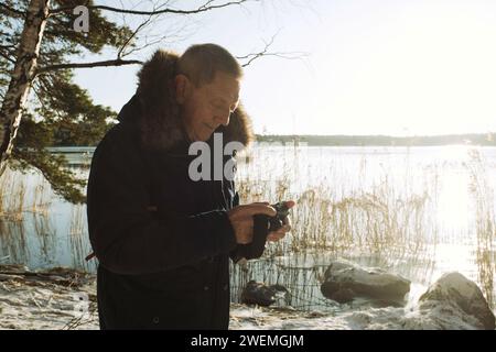retired man looking at his camera taking pictures of a lake in Sweden Stock Photo