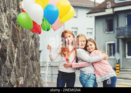 Outdoor portrait of 3 cute little girls with colorful balloons, wearing sweatshirts Stock Photo