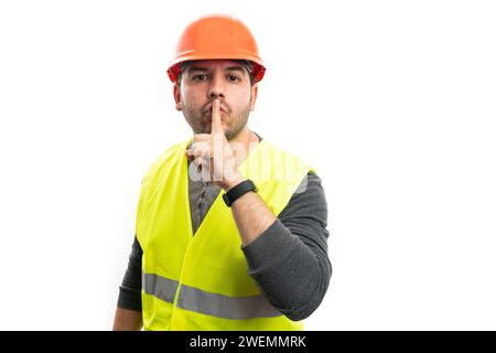 Adult constructor man in work attire safety helmet fluorescent vest making shush gesture with index finger over mouth as secret concept isolated on wh Stock Photo