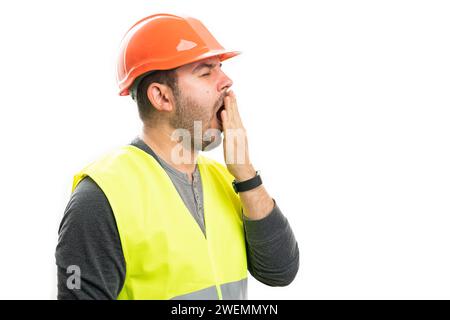Tired adult male constructor covering mouth as yawning sleepy wearing work clothing fluorescent vest and orange safety mask isolated on white backgrou Stock Photo