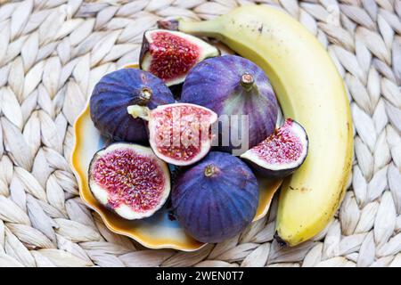Still life of Fresh Figs lying on a plate with yellow edges, whole and cut into pieces Stock Photo